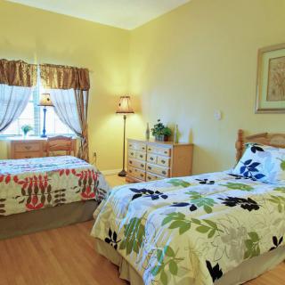 A cozy bedroom featuring twin beds with floral bedding, warmly lit by lamps and softened by drapes over the window.