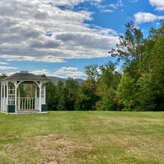 A serene landscape featuring a white gazebo surrounded by lush greenery under a partly cloudy sky.