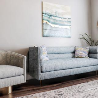 A stylish living room featuring a plush gray sofa and an elegant armchair, adorned with decorative pillows and complemented by abstract wall art.