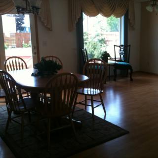 A cozy dining room with a wooden table, chairs, and large window letting in natural light.