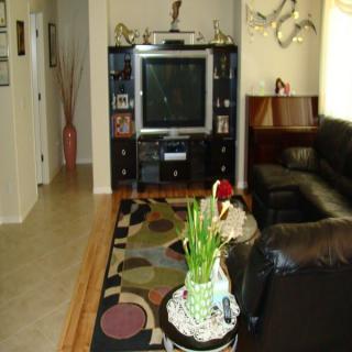 A cozy living room with a large television, entertainment center, and comfortable seating, featuring decorative elements and plants.