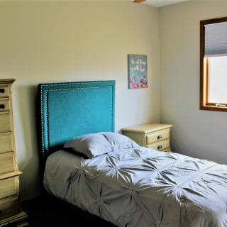 A cozy bedroom with a single bed, teal headboard, dresser, and window.