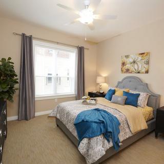 A cozy bedroom with stylish decor featuring a neatly made bed, curtains framing a large window, and a small lamp adding warmth to the room.