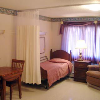 A cozy hospital room featuring a bed, chair, table, and soft lighting.