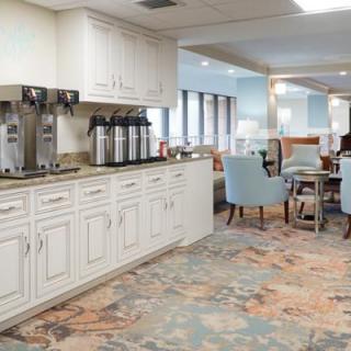 A cozy kitchen and dining area featuring a coffee station, white cabinets, carpeted flooring, and comfortable seating.