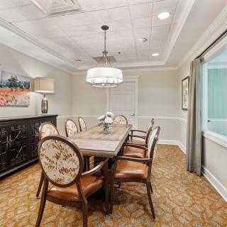 A well-appointed dining or conference room with a central wooden table, surrounded by upholstered chairs, featuring a chandelier above and artwork on the walls.