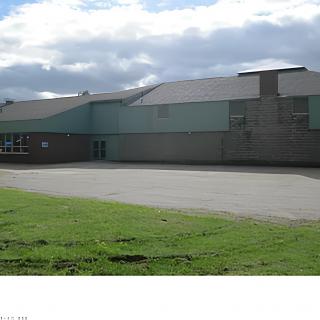 A view of a school building with a paved playground and grassy area under a cloudy sky.