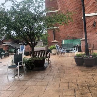 A cozy outdoor seating area featuring a variety of chairs and tables, surrounded by greenery, on a rainy day.