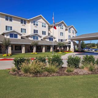 A large residential building surrounded by well-maintained landscaping under a clear blue sky.