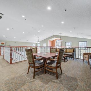 A spacious indoor seating area with a table and chairs, featuring carpeted flooring and ceiling lighting.