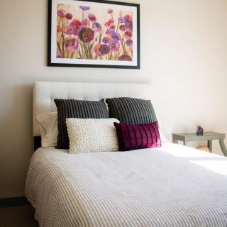 A neatly arranged bedroom with a bed, decorative pillows, and floral artwork on the wall.
