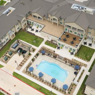 Aerial view of an apartment complex featuring a central swimming pool and outdoor seating area.