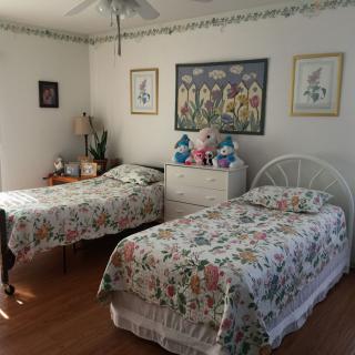 A cozy bedroom with twin beds featuring floral bedding, decorated with wall art and a small dresser.