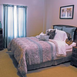 A cozy bedroom featuring a neatly made bed with decorative pillows and soft lighting from the windows.