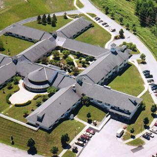 An aerial view of a complex featuring a distinctive architectural layout, surrounded by green spaces.