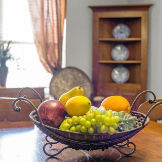 A fruit basket with grapes, an orange, a pomegranate, and a lemon on a wooden table in a cozy home setting.