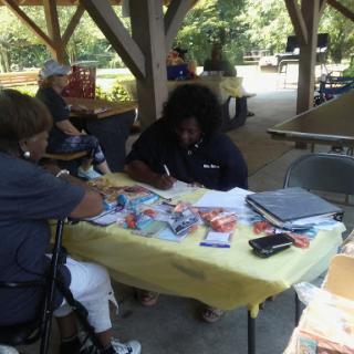 A community gathering taking place under a pavilion, with individuals engaged in activities at a table.