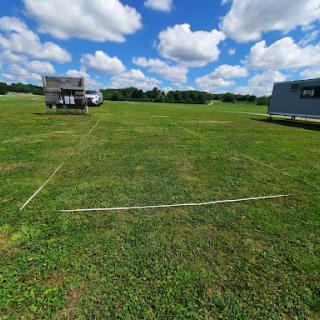 A scenic view of a grassy field with vehicles parked nearby under a blue sky filled with fluffy clouds.