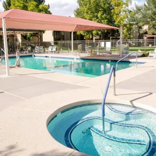 An outdoor swimming pool area with a jacuzzi and sunshade, surrounded by trees.