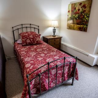 A cozy bedroom featuring a single bed with floral bedding, a bedside lamp, and decorative artwork on the wall.