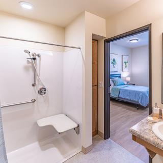 A modern hotel room with an accessible bathroom and adjoining bedroom.