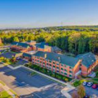 Aerial view of a large brick building surrounded by trees and parking lots.