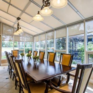 A spacious dining room with a long table and chairs, surrounded by large windows letting in natural light.