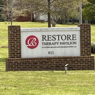 Sign for Restore Therapy Pavilion with brick base located outdoors.