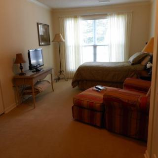 A cozy bedroom with a bed, TV, and armchair near a window.