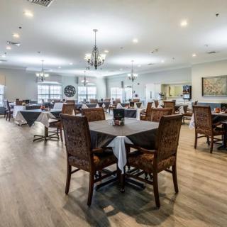 A spacious dining room with neatly arranged tables and chairs, adorned with chandeliers and wooden flooring.