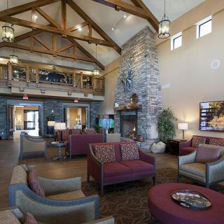 A spacious lobby with a modern design featuring comfortable seating, a stone fireplace, and wooden beam high ceilings.
