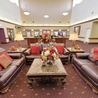 A spacious lobby area featuring leather sofas, a central coffee table adorned with floral arrangements, and ambient lighting from table lamps.