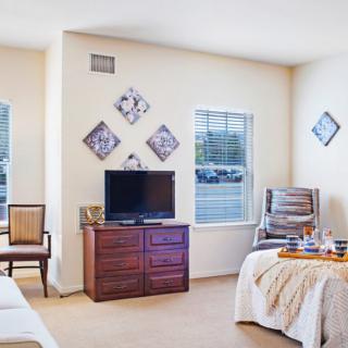 A bright and cozy living room with a television, comfortable chairs, and decorative wall art.