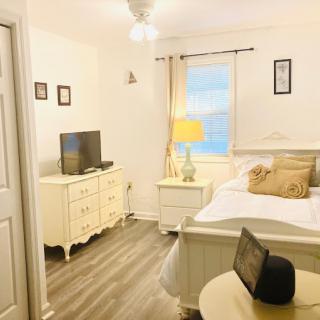 A cozy bedroom featuring a bed, TV, and nightstand with a lamp, complemented by wooden flooring and bright decor.