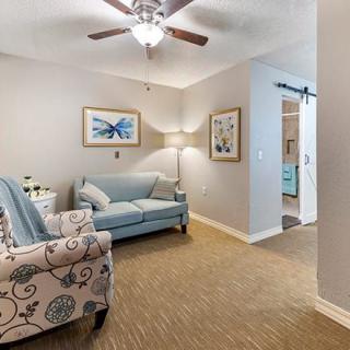 A cozy living room with a blue sofa, patterned armchair, ceiling fan, and decorative wall art.
