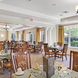A well-lit dining room with neatly arranged tables and chairs, featuring large windows and elegant decor.