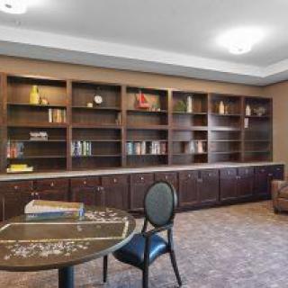 A cozy library room featuring tall bookshelves, a round table, and chairs.