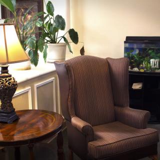 A cozy living room setup featuring an armchair, side table, and a lamp beside a fish tank.