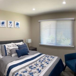 A modern and cozy bedroom with a neatly made bed, decorative pillows, artwork on the wall, and a window with blinds.