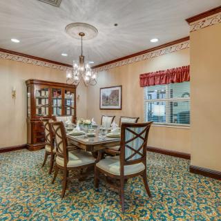An elegant dining room featuring a chandelier, dining table with chairs, and a china cabinet on a patterned carpet.