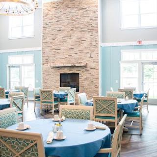 A bright and elegantly decorated dining area featuring round tables with blue tablecloths and a stone fireplace.