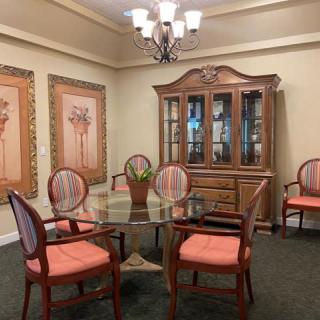 A traditional dining room with a glass table, upholstered chairs, and a decorative cabinet.