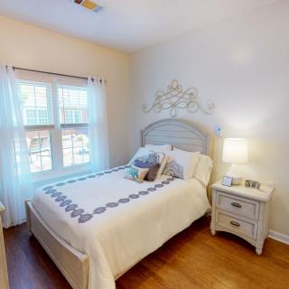 A cozy bedroom with a neatly made bed, nightstand, and lamp by the window.