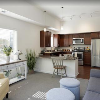 A modern open-concept kitchen and living area with stainless steel appliances, wood cabinets, and ample natural light.