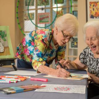 Two senior women enjoying a creative painting session together.