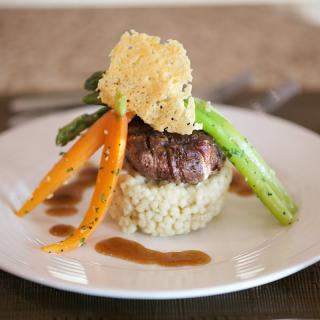 A beautifully plated gourmet dish featuring steak atop a bed of risotto, garnished with asparagus, carrots, and a crispy cheese topping.