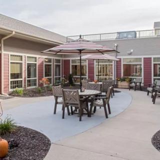 An outdoor patio area with tables, chairs, and umbrellas set in a courtyard surrounded by a building.