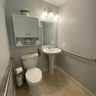 A modern and accessible bathroom featuring a toilet, sink, and safety grab bars.