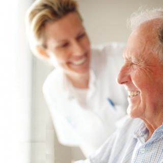 A caregiver smiling at an elderly man, depicting a moment of friendly interaction in a healthcare setting.
