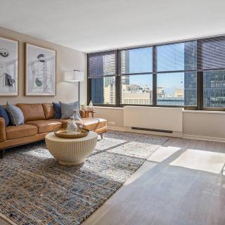 A modern living room with large windows offering a city view, featuring stylish furniture and contemporary decor.